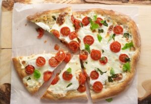 Sliced pizza with part skim mozzarella cheese, tomatoes and basil