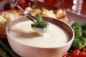 Broccoli being dipped into a bowl of swiss cheese fondue