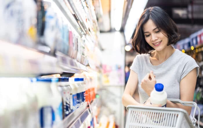 A woman in a grocery store smiling as she places a jug of milk in her basket.