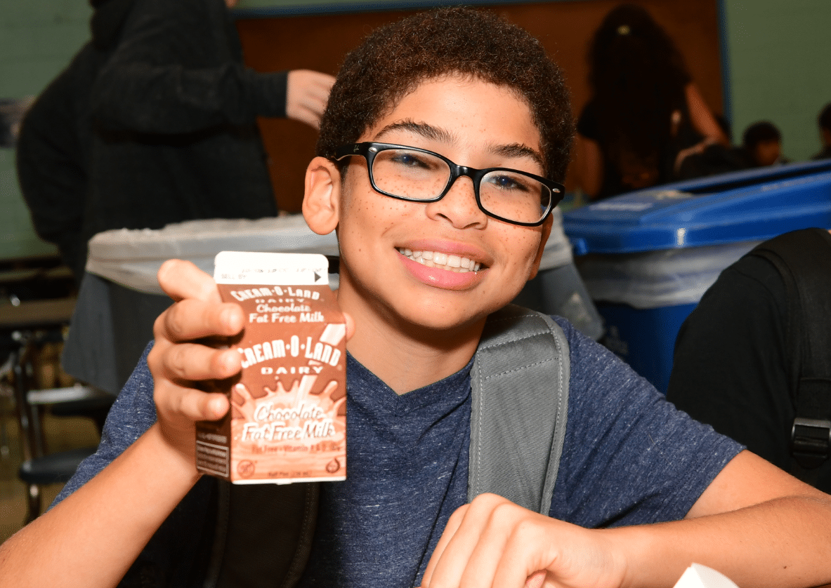 Young boy holding a carton of chocolate milk and smiling