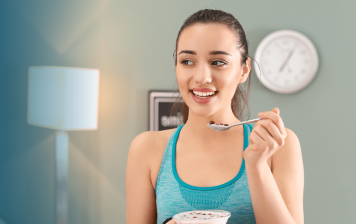 A woman holding a spoon and enjoying a yogurt with fruits after a home workout session.