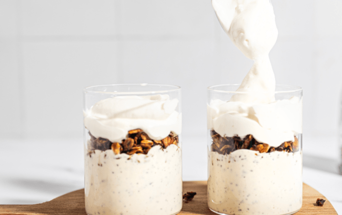 Two glass jars of greek yogurt parfait with a metal spoon dipping into the yogurt of the right side jar.