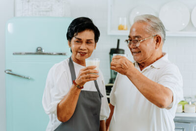 Happy Asian senior couple drinking milk at home. 70s Elderly married man and woman holding a glass of milk at kitchen